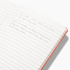 Close up of the Everyday Notebook in Lined open with writing on it on a white background. 