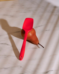 The GIR 3 Piece Mini Tool Set Red Mini Spoonula resting on a pear on a marble surface. 