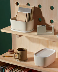 Two Small Cream Storage bins, one with books in it one with a plastic lid on a wooden shelf.