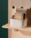 Close up of a Small Cream Storage bin with books in it on a wooden shelf.
