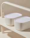 Two Small Cream Storage Bins with plastic lids on a cream background. 