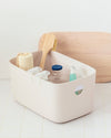 An Open Spaces Large Cream Storage bin with cleaning supplies inside it on a white background.
