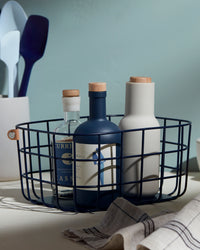 The Open Spaces Navy Medium Wire Basket with bottles inside it on a blue background.