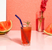 A straw from the Glass Straws in Cool Set in a glass of watermelon juice with half a water melon in the left and right. 