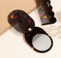 A close up of the 2 in 1 Pocket Comb Mirror in Black Amber on a cream background. 