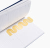 Brass Bookmark in Wave inside a Planner on a white background. 