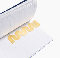Brass Bookmark in Wave inside a Planner on a white background. 