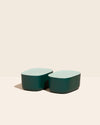 Two Small Dark Green Storages Bins with plastic Mint lids on a cream background.