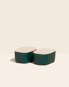 Two Small Dark Green Storages Bins with wooden lids on a cream background.