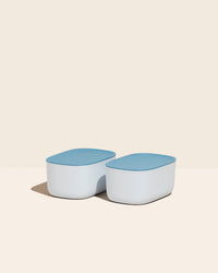 Two Small Light Blue Storages Bins with plastic dark blue lids on a cream background.