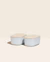 Two Small Light Blue Storages Bins with wooden lids on a cream background.