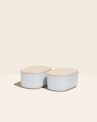 Two Small Light Blue Storages Bins with wooden lids on a cream background.