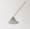 The Gray Glass Meso Incense Holder with a incense in it on a grayish background.