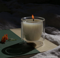 A 6 oz Citronella  Double wall Candle on a dark background with a small flower on the left. 