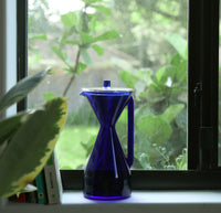 The Cobalt Pour Over Carafe with greenery in the background. 